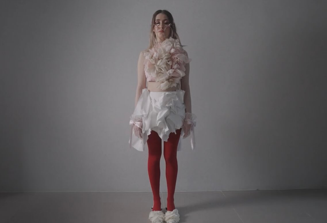 Film still: Dalia standing against a grey backdrop in the pinned tulle look