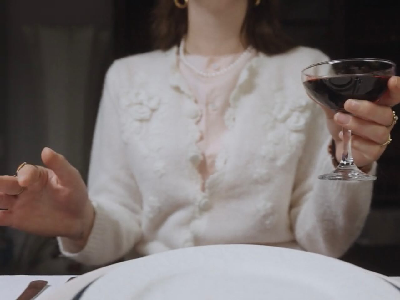 Film still: a hand raising a glass of red wine at the dinner table